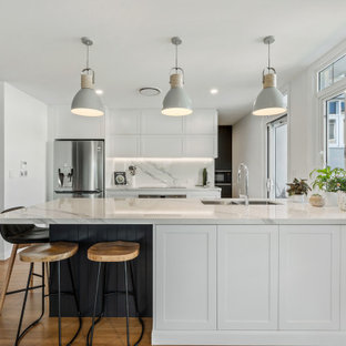 Design ideas for a beach style galley kitchen in Central Coast with an undermount sink, shaker cabinets, white cabinets, white splashback, stainless steel appliances, medium hardwood floors, a peninsula, brown floor and white benchtop.