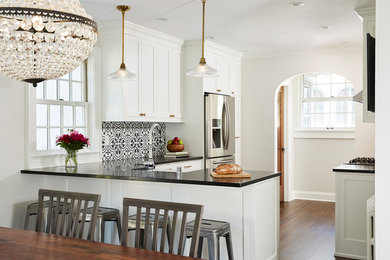 Eat-in kitchen - large country medium tone wood floor and brown floor eat-in kitchen idea in Minneapolis with a farmhouse sink, flat-panel cabinets, white cabinets, soapstone countertops, stainless steel appliances, a peninsula and black countertops