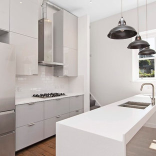 This is an example of a contemporary kitchen in London with a double-bowl sink, flat-panel cabinets, grey cabinets, white splashback, metro tiled splashback, stainless steel appliances, medium hardwood flooring, a breakfast bar and white worktops.