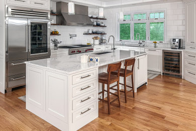 Example of a mid-sized minimalist l-shaped medium tone wood floor and brown floor eat-in kitchen design in Boston with recessed-panel cabinets, white cabinets, marble countertops, white backsplash, stainless steel appliances, an island, white countertops and an undermount sink