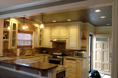 Inspiration for a mid-sized timeless u-shaped medium tone wood floor eat-in kitchen remodel in Oklahoma City with a double-bowl sink, raised-panel cabinets, distressed cabinets, granite countertops, multicolored backsplash, ceramic backsplash and stainless steel appliances