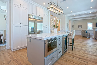 Eat-in kitchen - large transitional u-shaped medium tone wood floor and brown floor eat-in kitchen idea in Los Angeles with an island, a farmhouse sink, recessed-panel cabinets, white cabinets, quartzite countertops, white backsplash, stone slab backsplash, stainless steel appliances and white countertops