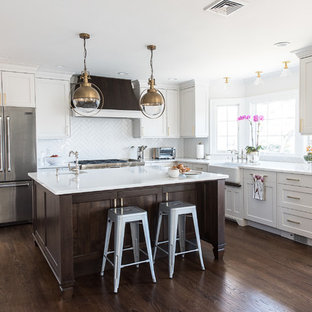 Foto de cocina comedor en L, clásica renovada, de tamaño medio, con fregadero sobremueble, puertas de armario blancas, salpicadero blanco, electrodomésticos de acero inoxidable, una isla, suelo marrón, armarios con paneles lisos, encimera de cuarzo compacto, salpicadero de azulejos de cerámica, suelo de madera en tonos medios y encimeras blancas