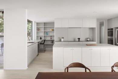 Modern u-shaped kitchen/diner in Austin with a submerged sink, flat-panel cabinets, white cabinets, stainless steel appliances, light hardwood flooring, an island, beige floors and grey worktops.