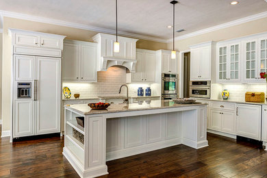 Inspiration for a mid-sized transitional l-shaped dark wood floor and brown floor kitchen remodel in Other with a farmhouse sink, shaker cabinets, white cabinets, granite countertops, white backsplash, ceramic backsplash, paneled appliances and an island