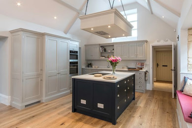 Inspiration for a medium sized classic open plan kitchen in Gloucestershire with a double-bowl sink, flat-panel cabinets, quartz worktops, stainless steel appliances, medium hardwood flooring and an island.