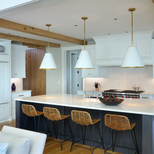 Expansive transitional l-shaped open plan kitchen in Grand Rapids with a farmhouse sink, recessed-panel cabinets, white cabinets, granite benchtops, white splashback, granite splashback, panelled appliances, light hardwood floors, with island, white benchtop and brown floor.