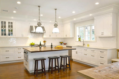 Kitchen - mid-sized transitional l-shaped medium tone wood floor kitchen idea in New York with raised-panel cabinets, white cabinets, marble countertops, white backsplash, stainless steel appliances, a single-bowl sink and an island