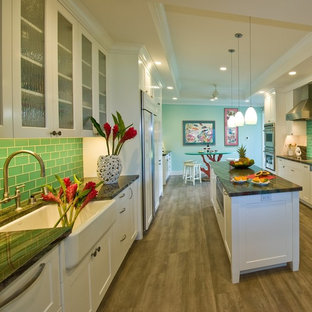 Tropical kitchen in Hawaii with a farmhouse sink, shaker cabinets, white cabinets, granite benchtops, green splashback, glass tile splashback, panelled appliances, vinyl floors and with island.