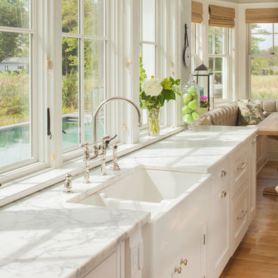Example of a large beach style light wood floor eat-in kitchen design in New York with a farmhouse sink, recessed-panel cabinets, white cabinets, marble countertops, white countertops and window backsplash