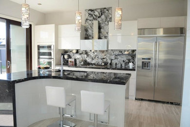 Example of a minimalist galley travertine floor eat-in kitchen design in Other with an undermount sink, flat-panel cabinets, white cabinets, granite countertops, glass sheet backsplash, stainless steel appliances and an island