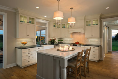 Example of a large arts and crafts l-shaped light wood floor and brown floor eat-in kitchen design in Boston with a farmhouse sink, shaker cabinets, white cabinets, white backsplash, ceramic backsplash, stainless steel appliances, an island and marble countertops