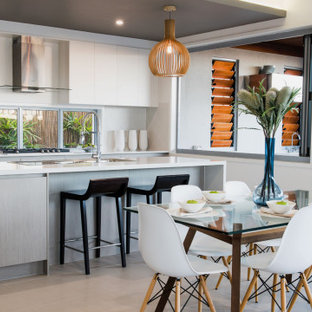 This is an example of a contemporary l-shaped kitchen in Brisbane with flat-panel cabinets, white cabinets, window splashback, with island, grey floor and white benchtop.