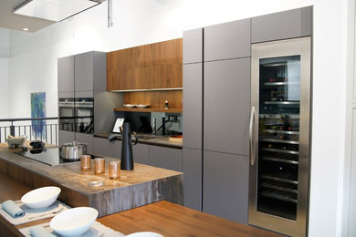 Photo of a large modern single-wall kitchen/diner in London with a single-bowl sink, grey cabinets, metallic splashback, mirror splashback, stainless steel appliances, an island and brown worktops.