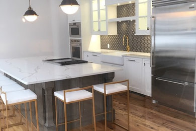 Expansive classic single-wall kitchen/diner in Bridgeport with a belfast sink, shaker cabinets, white cabinets, engineered stone countertops, brown splashback, ceramic splashback, stainless steel appliances, light hardwood flooring, an island, yellow floors and white worktops.