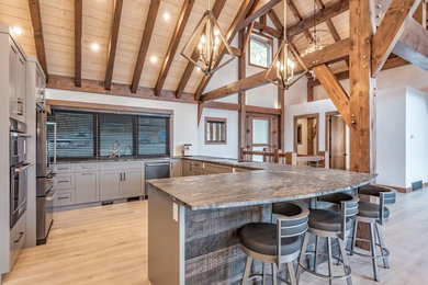 Example of a large arts and crafts u-shaped light wood floor and beige floor open concept kitchen design in Other with an undermount sink, stainless steel appliances, shaker cabinets, brown cabinets and a peninsula