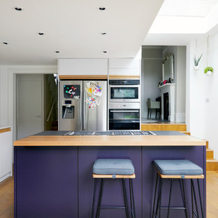 Idée de décoration pour une grand cuisine américaine design en L avec un évier intégré, un placard à porte plane, des portes de placard violettes, un plan de travail en surface solide, une crédence blanche, une crédence en dalle de pierre, un électroménager en acier inoxydable, un sol en bois brun, un îlot central et un sol marron.