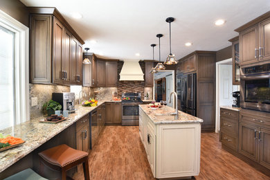 Large arts and crafts l-shaped vinyl floor and brown floor enclosed kitchen photo in Other with an undermount sink, recessed-panel cabinets, medium tone wood cabinets, granite countertops, beige backsplash, stone slab backsplash, stainless steel appliances, an island and beige countertops