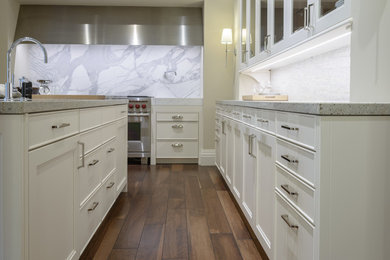 Large transitional l-shaped medium tone wood floor and brown floor enclosed kitchen photo in Toronto with white cabinets, granite countertops, stainless steel appliances, an island, an undermount sink, glass-front cabinets, white backsplash and stone slab backsplash