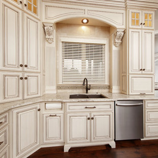 Foto de cocina en U, clásica renovada, de tamaño medio, cerrada, con fregadero bajoencimera, armarios con paneles con relieve, puertas de armario blancas, encimera de granito, salpicadero beige, salpicadero de travertino, electrodomésticos de acero inoxidable, suelo de madera oscura y suelo marrón
