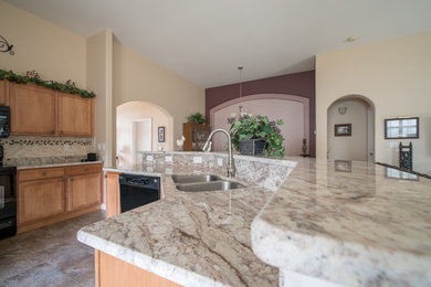 This is an example of a medium sized traditional l-shaped open plan kitchen in Raleigh with a double-bowl sink, recessed-panel cabinets, light wood cabinets, granite worktops, grey splashback, stone slab splashback, black appliances, ceramic flooring, an island, grey floors and grey worktops.