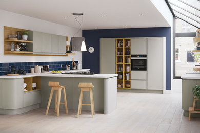Medium sized contemporary u-shaped open plan kitchen in Oxfordshire with flat-panel cabinets, grey cabinets, composite countertops, blue splashback, ceramic splashback, black appliances and white worktops.