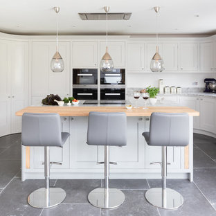 Large classic kitchen in Surrey with shaker cabinets, black appliances, an island, grey floors, a submerged sink and white cabinets.