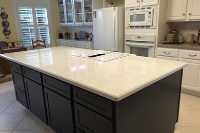 Example of a mid-sized classic l-shaped travertine floor eat-in kitchen design in Austin with a double-bowl sink, raised-panel cabinets, white cabinets, quartz countertops, white backsplash, ceramic backsplash, white appliances and an island