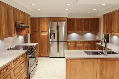 Example of a mid-sized classic u-shaped vinyl floor enclosed kitchen design in Vancouver with an undermount sink, raised-panel cabinets, medium tone wood cabinets, quartz countertops, beige backsplash, subway tile backsplash, stainless steel appliances and a peninsula
