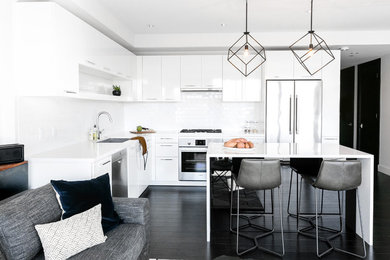 Example of a large trendy l-shaped dark wood floor and black floor eat-in kitchen design in Phoenix with an undermount sink, flat-panel cabinets, white cabinets, quartz countertops, white backsplash, subway tile backsplash, stainless steel appliances, an island and white countertops