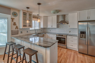 Inspiration for a large transitional u-shaped eat-in kitchen remodel in St Louis with a farmhouse sink, shaker cabinets, white cabinets, granite countertops, white backsplash, subway tile backsplash, stainless steel appliances, a peninsula and multicolored countertops