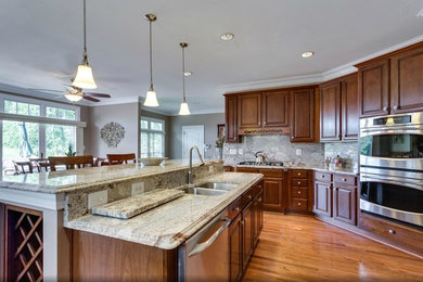 Arts and crafts u-shaped medium tone wood floor eat-in kitchen photo in DC Metro with raised-panel cabinets, medium tone wood cabinets, granite countertops, stone slab backsplash, stainless steel appliances and an island