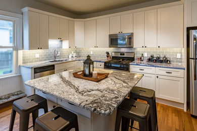 Example of a mid-sized transitional l-shaped medium tone wood floor eat-in kitchen design in St Louis with an undermount sink, shaker cabinets, white cabinets, granite countertops, gray backsplash, subway tile backsplash, stainless steel appliances, an island and multicolored countertops
