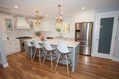 Eat-in kitchen - mid-sized transitional l-shaped brown floor eat-in kitchen idea in Vancouver with an undermount sink, shaker cabinets, white cabinets, quartz countertops, white backsplash, ceramic backsplash, stainless steel appliances, an island and white countertops