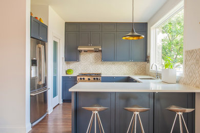 Esempio di una cucina minimal di medie dimensioni con ante in stile shaker, top in superficie solida, paraspruzzi beige, paraspruzzi con piastrelle in ceramica, elettrodomestici in acciaio inossidabile, pavimento in legno massello medio, lavello sottopiano, ante blu e penisola