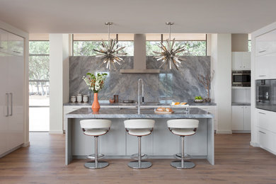Inspiration for a contemporary light wood floor and beige floor kitchen remodel in Austin with an undermount sink, flat-panel cabinets, white cabinets, gray backsplash, stone slab backsplash, stainless steel appliances, an island and gray countertops