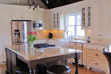 Inspiration for a mid-sized transitional l-shaped light wood floor kitchen remodel in New York with a farmhouse sink, recessed-panel cabinets, white cabinets, granite countertops, beige backsplash, mosaic tile backsplash, stainless steel appliances and an island