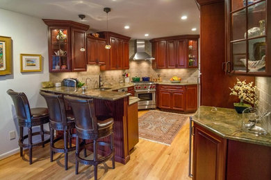 Example of a mid-sized classic u-shaped medium tone wood floor eat-in kitchen design in Newark with an undermount sink, raised-panel cabinets, granite countertops, beige backsplash, stainless steel appliances, a peninsula, dark wood cabinets and stone tile backsplash