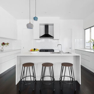 Mid-sized contemporary u-shaped kitchen in Melbourne with a double-bowl sink, white cabinets, granite benchtops, white splashback, subway tile splashback, black appliances, dark hardwood floors, with island, black floor, white benchtop and flat-panel cabinets.