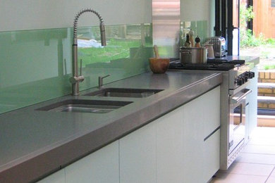 Inspiration for a large modern open plan kitchen in London with a submerged sink, flat-panel cabinets, concrete worktops, green splashback, glass sheet splashback, stainless steel appliances, ceramic flooring and an island.
