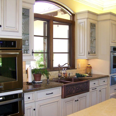 Example of a large classic l-shaped ceramic tile and beige floor open concept kitchen design in San Diego with stainless steel appliances, a farmhouse sink, marble countertops, white cabinets, beige backsplash, stone tile backsplash, raised-panel cabinets and two islands