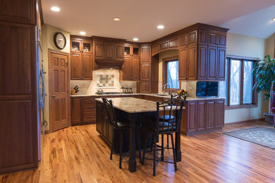 Mid-sized elegant u-shaped light wood floor kitchen photo in Other with a double-bowl sink, raised-panel cabinets, medium tone wood cabinets, granite countertops, beige backsplash, stone tile backsplash, stainless steel appliances and an island