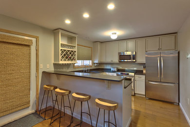 Example of a mid-sized transitional u-shaped light wood floor and brown floor kitchen design in Burlington with shaker cabinets, white cabinets, solid surface countertops, stainless steel appliances and a peninsula