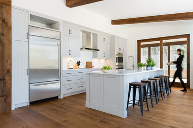 Modern inredning av ett stort kök, med en dubbel diskho, skåp i shakerstil, grå skåp, bänkskiva i kvarts, vitt stänkskydd, stänkskydd i tunnelbanekakel, rostfria vitvaror, mellanmörkt trägolv och en köksö