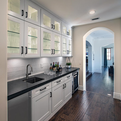 Inspiration for a transitional single-wall dark wood floor and brown floor kitchen pantry remodel in Orange County with an undermount sink, glass-front cabinets, white cabinets, white backsplash, subway tile backsplash, no island and black countertops