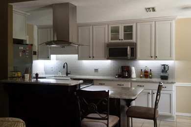 Medium sized classic u-shaped kitchen/diner in Birmingham with a belfast sink, shaker cabinets, white cabinets, granite worktops, white splashback, metro tiled splashback, stainless steel appliances, travertine flooring and an island.