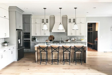 Example of a transitional l-shaped light wood floor eat-in kitchen design in Indianapolis with a single-bowl sink, shaker cabinets, quartz countertops, ceramic backsplash, stainless steel appliances, an island and white countertops