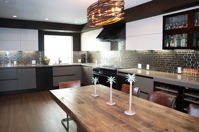 This is an example of a large contemporary u-shaped kitchen/diner in Los Angeles with an integrated sink, flat-panel cabinets, beige cabinets, engineered stone countertops, metallic splashback, glass tiled splashback, black appliances, medium hardwood flooring, no island, brown floors and beige worktops.
