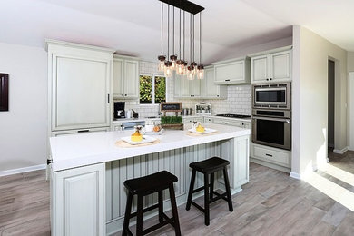 Example of a mid-sized beach style u-shaped medium tone wood floor eat-in kitchen design in Orange County with a double-bowl sink, raised-panel cabinets, white cabinets, soapstone countertops, white backsplash, subway tile backsplash, stainless steel appliances and an island