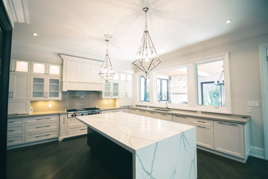 Large transitional u-shaped dark wood floor and brown floor eat-in kitchen photo in Toronto with an undermount sink, shaker cabinets, white cabinets, gray backsplash, paneled appliances, an island and marble countertops